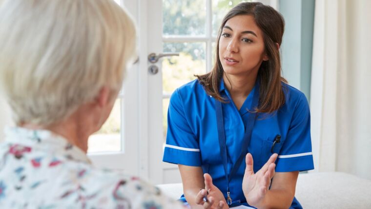 Senior woman talking to young care nurse on home visit